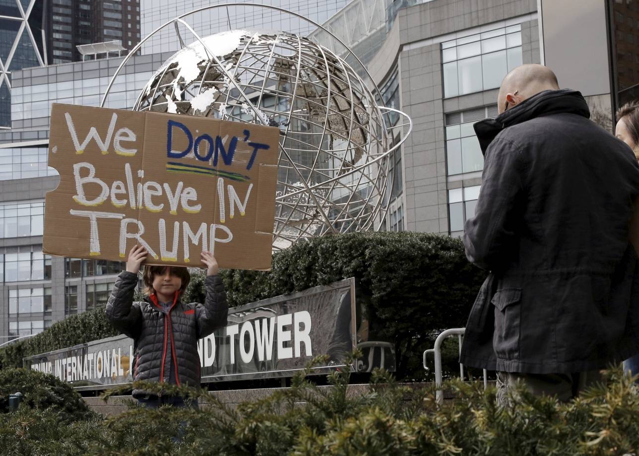 Мальчитк с антитрамповским плакатом на фоне Trump International Hotel and Tower